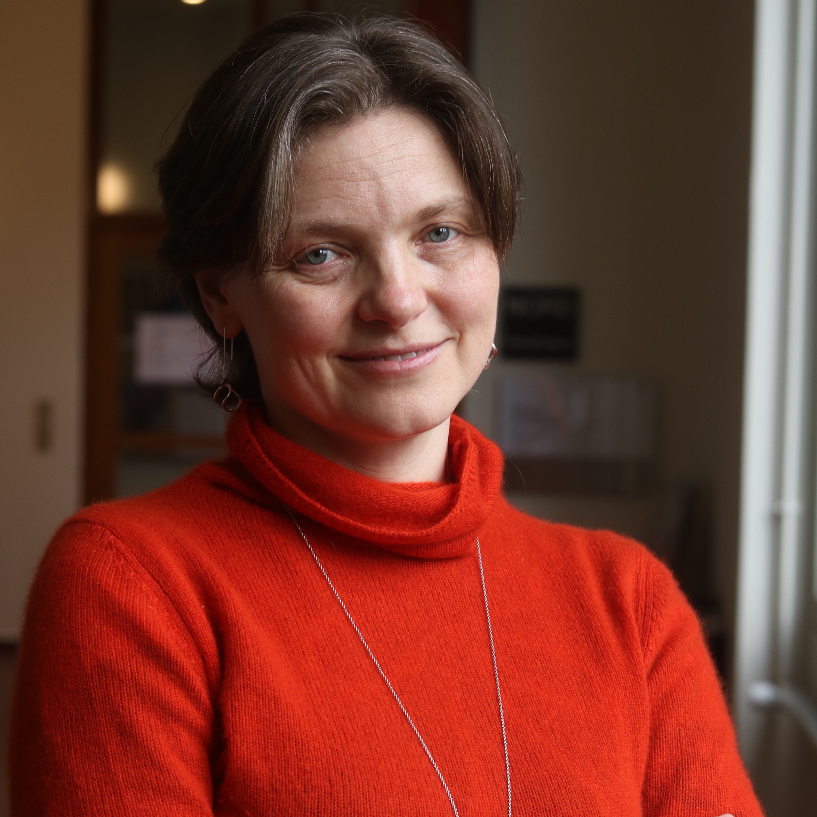 Photo of Irina Shklovsk wearing a red turtle neck and smiling towards the camera.