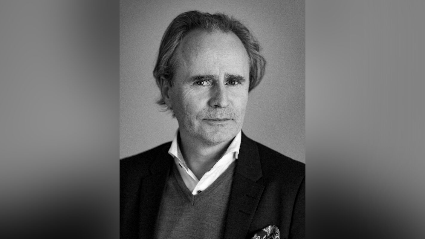 Christofer Black and white photo of a man in a dark suit in front of a plain background.