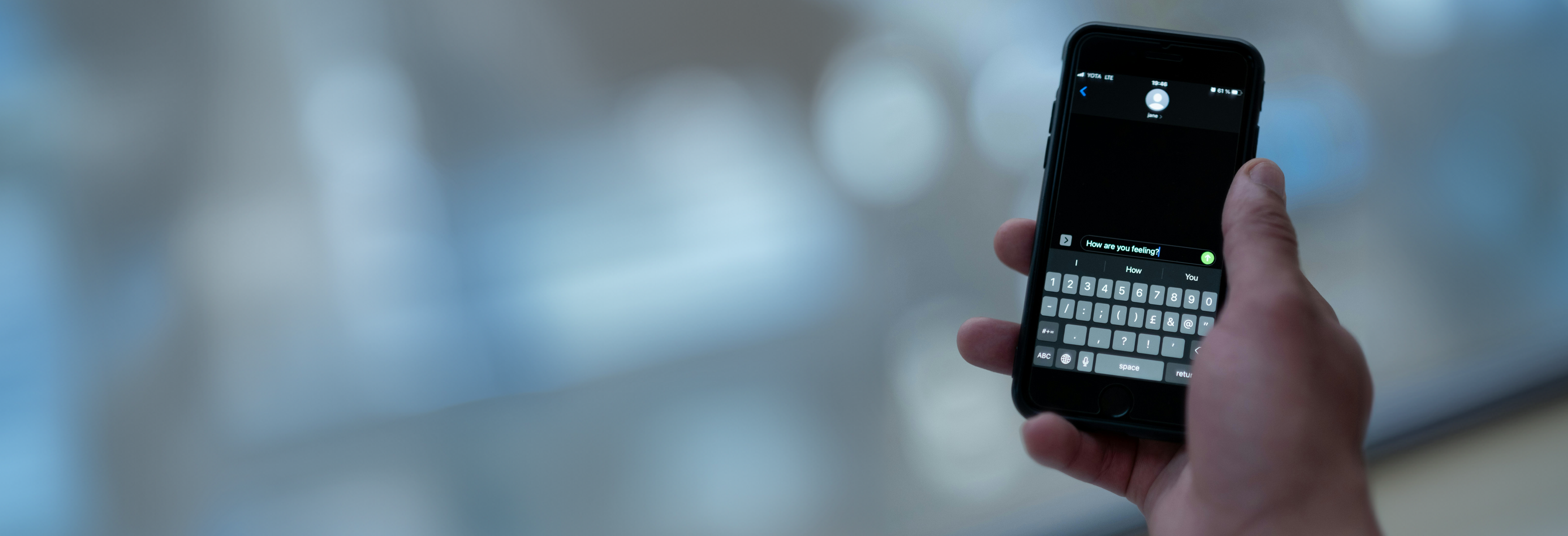 Image of a hand holding a phone. A chat application is open on the phone. The interface is black with white text. Implications that the hand holding the phone has just written the words "How are you doing?". Photo by Ron Lanch on Pexels.