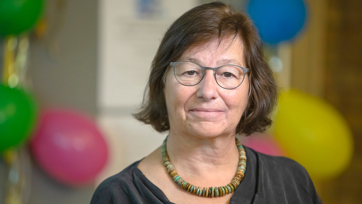 Kerstin Sahlin. Glad kvinna med glasögon framför blå, gula och rosa ballonger.