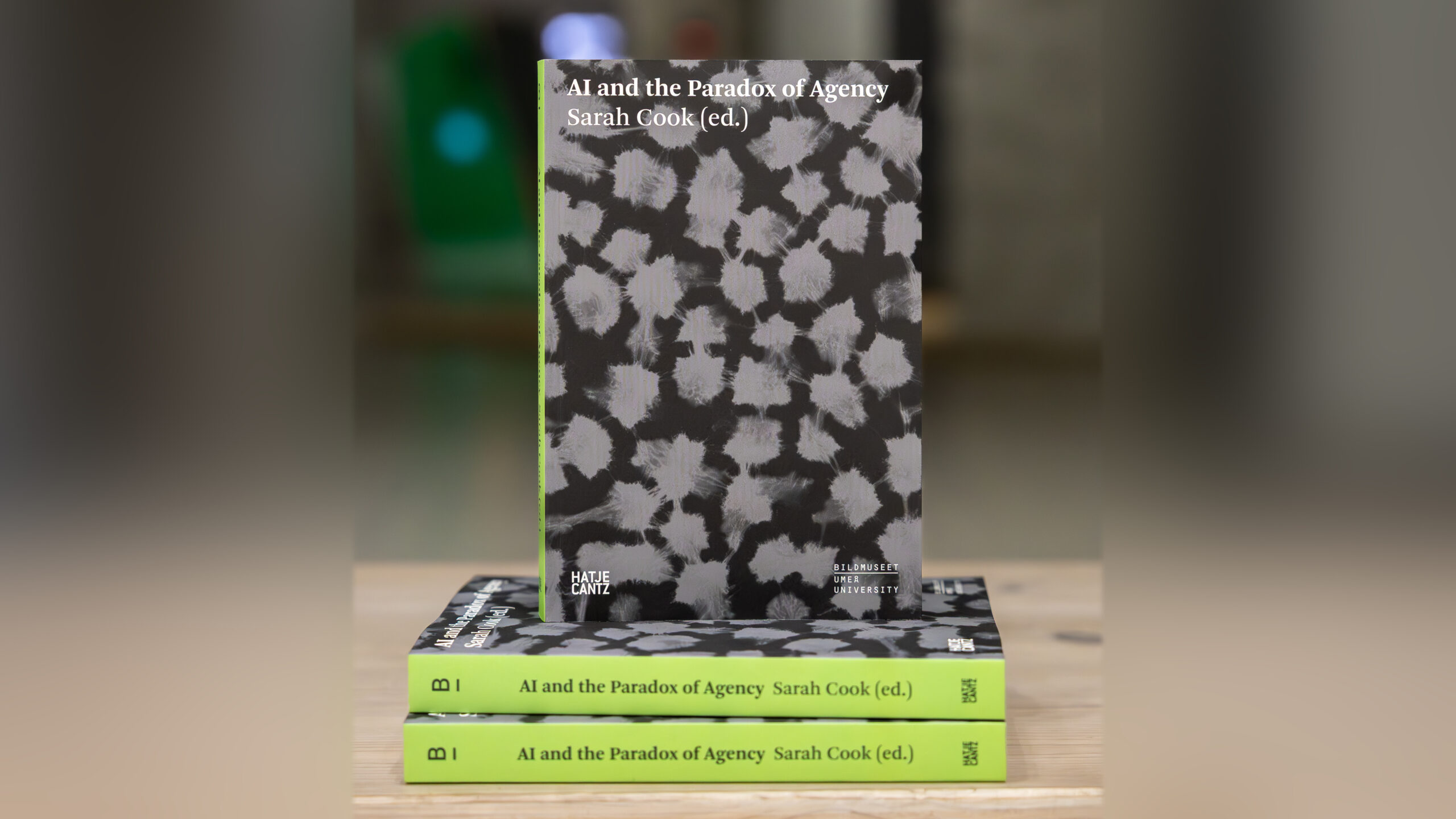 Three black and white marbled books with a lime green spine stacked on top of a wooden table.
